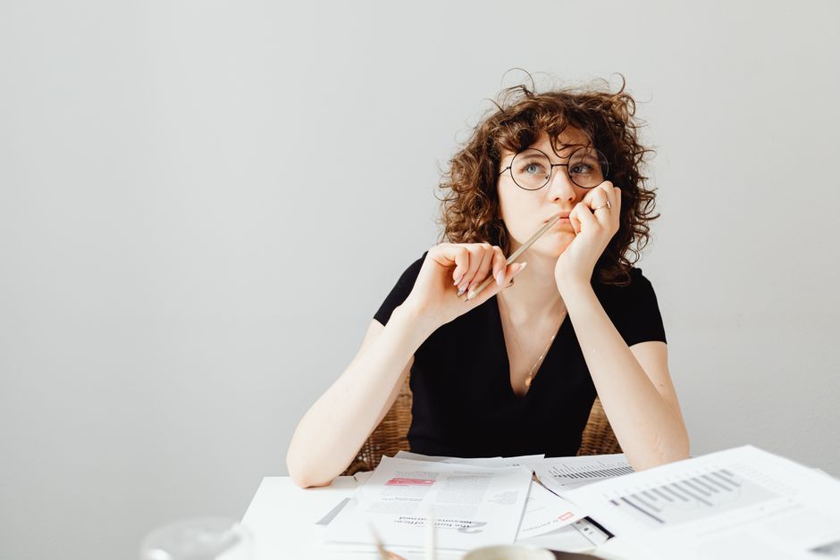 Someone sitting at a desk covered in paperwork, thinking.