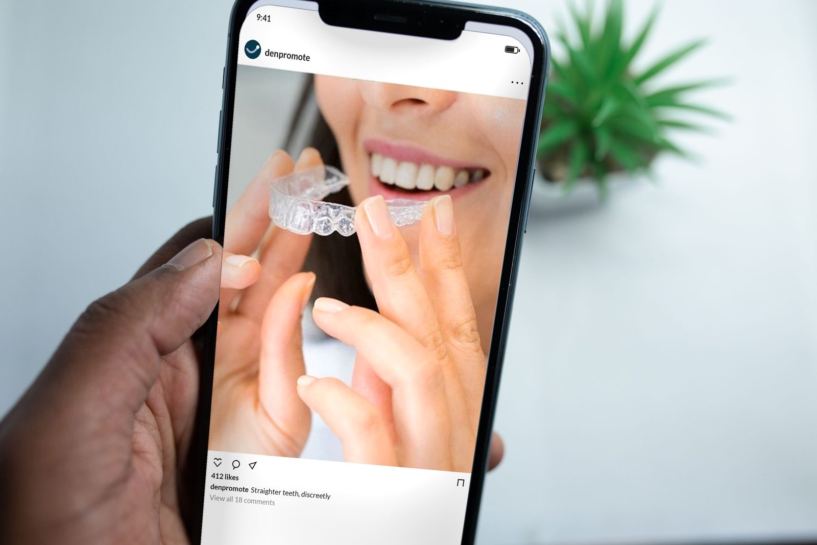 A hand holding a phone showing an Instagram post from a dental practice of a woman fitting a clear aligner over her teeth.