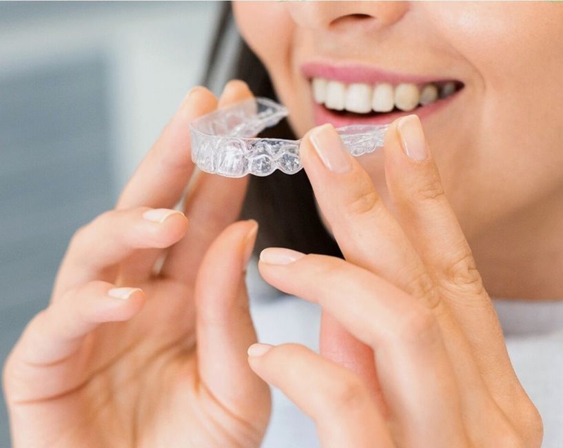 A woman holding a clear aligner up to her mouth, smiling.