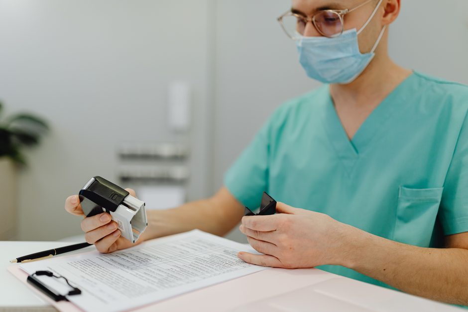A clinician in scrubs checking patient paperwork against a clipboard.