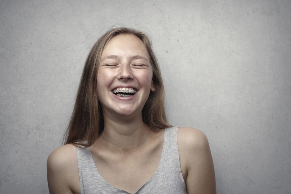 A woman laughing, head back, against a plain grey wall.