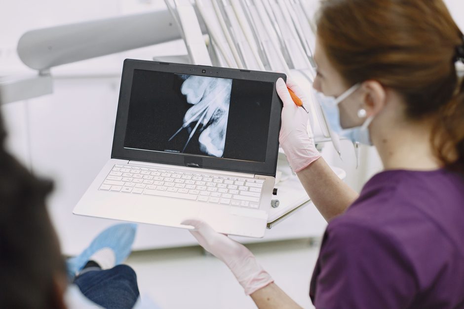 A dentist showing a patient their x-ray results on a laptop in a treatment room.
